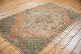 Distressed Oushak rug corner with teal starburst spandrel, pale terra cotta and beige border pattern.
