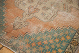 Distressed vintage Oushak rug showing terra cotta, teal starbursts, and serrated geometric border.