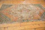 Worn corner of a distressed vintage Oushak rug with teal starburst spandrel and pale terra cotta field.