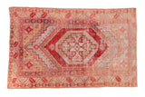 Distressed Oushak rug with cherry red stepped hexagonal medallion on a faded beige field.