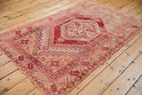 Distressed Oushak rug corner with cherry red serrated leaf border and blush-beige field.