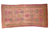 Distressed Oushak runner features a dusty rose field with bold purple, green, and yellow motifs.