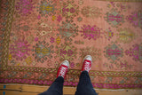 Distressed vintage Oushak runner featuring a blush background and vibrant purple floral gul motifs.