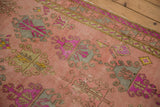 Distressed Oushak rug texture, highlighting floral gul motifs with wear, dusty rose, purple, mint green.