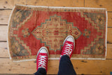 Distressed vintage Oushak mat with low pile, cherry red geometric pattern and slight bowed contour.