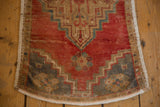 Bowed end of distressed vintage Oushak rug, showing low pile, fringe, and floral finials.