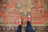 Distressed brick red Oushak carpet showcasing worn texture and Rococo-inspired floral roundel motifs.