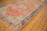 Distressed Oushak rug corner showcases faded brick red field and intricate blue floral border.