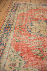 Distressed brick red Oushak rug pile with royal blue border, floral vines, and wear.