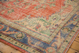 Faded brick red Oushak rug with blue border and ivory floral vine motifs.