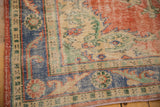 Distressed hand-knotted Oushak rug corner with brick red, blue border, and green floral motifs.