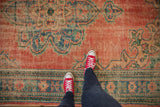 Distressed vintage Oushak carpet with abrashed brick red field and vivid blue-green motifs.