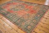 Distressed Oushak rug corner with brick red and denim blue patterns, highlighting even wear.