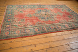 Vintage distressed Oushak rug corner showing worn brick red field and denim blue border.
