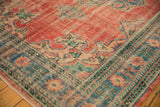 Corner view of distressed Oushak rug showing faded brick red field and intricate blue-green border.