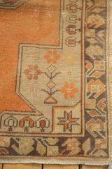 Distressed Oushak rug corner detail: tangerine orange field, beige geometric vinery, faint foundation.