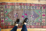 Distressed Oushak rug's faded bronze pile with vibrant pink floral motifs.