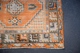 Distressed vintage Oushak rug corner with faded tangerine field, geometric borders, and white fringe.
