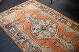 Distressed vintage Oushak rug with faded tangerine, ivory, and silver geometric patterns.