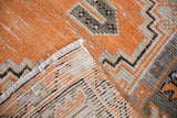 Folded vintage Oushak rug, revealing distressed tangerine pile, woven foundation, and fringe.