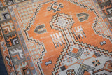 Visible wear on faded tangerine, antique ivory geometric animal motifs of the Oushak rug.