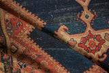 Worn pile of a folded Antique Malayer rug with abrashed indigo and tomato red geometric motifs.