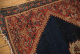 Worn corner of antique Malayer rug, showing secured edge with wear, geometric red border, and indigo field.