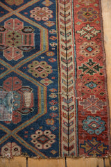 Antique Kurdish rug detail: navy geometric field, germinating plant border, red floral outer border, visible patch.