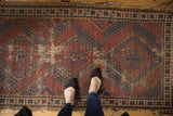 Antique Caucasian rug showing significant pile wear, tattered edges, red and navy geometric pattern.