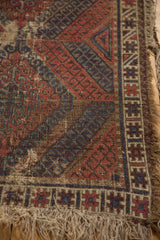Antique Caucasian rug with worn pile, tattered fringe, overcast edges, geometric red and navy patterns.
