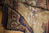 Close-up of folded antique Serab rug, displaying meandering vine and pawn borders with wear.