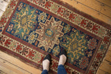 Antique Caucasian rug corner, geometric motifs, indigo field, cherry red floral border, subtle pile variation.