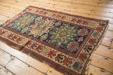 Oversized floral blossom border with alternating colors on an antique Caucasian rug's geometric field.
