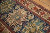 Antique Caucasian rug: geometric field, cherry red floral border, time-softened texture.