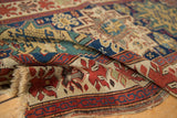 Antique Caucasian rug with cherry red floral border, geometric patterns, and fringed end.