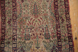 Detail of the antique Kerman rug showing blossomed foliage, cochineal red, navy, and even pile wear.