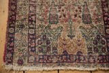 Antique Kerman rug close-up: cochineal red, navy border, worn pile, secured side, and lost fringe.