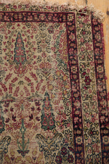 Antique Kerman rug corner with worn fringe, displaying cochineal red and ivory floral motifs.