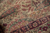 Detail of antique Kerman rug: Hand-knotted texture, cochineal red foliage on ivory, showing even wear.