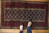 Vintage Belouch rug corner: beige geometric gul on navy, cherry red border, wave motif.