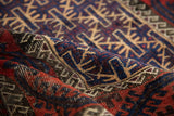 Curled view of vintage Belouch rug, showcasing geometric gul motifs in cherry red and navy.