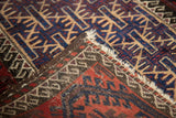 Vintage Belouch rug corner: red, navy geometric gul, hand-knotted foundation, overcast stitching.