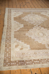 Distressed vintage Oushak rug corner with low pile, wear, and geometric patterns in beige, ivory, mauve.