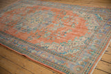 Distressed vintage Oushak carpet with worn tangerine, pale blue, and mint green floral design.