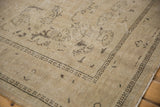 Distressed vintage Oushak rug corner, revealing worn sand field and faded brown leaf patterns.