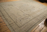 Vintage distressed Oushak carpet with even wear, faded sand tones, and subtle curvilinear motifs.