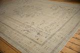 Distressed Oushak carpet corner with faded grape bunches and floral motifs in sand and brown.