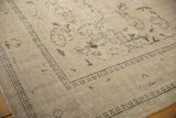 Distressed Oushak rug corner with even wear, faded grape and leaf motifs in sand and brown.
