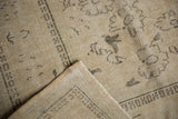 Distressed vintage Oushak rug corner, showing even pile wear, exposed foundation, and beige patterns.