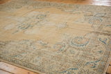 Distressed Oushak rug corner featuring faded European scrolling vines in ivory, green, and brown.